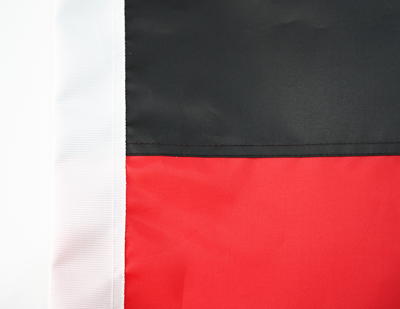 Close-up of a 210D polyester flag showing tight weave, reinforced stitching at the hem, and a metal grommet, with a background of a clear blue sky