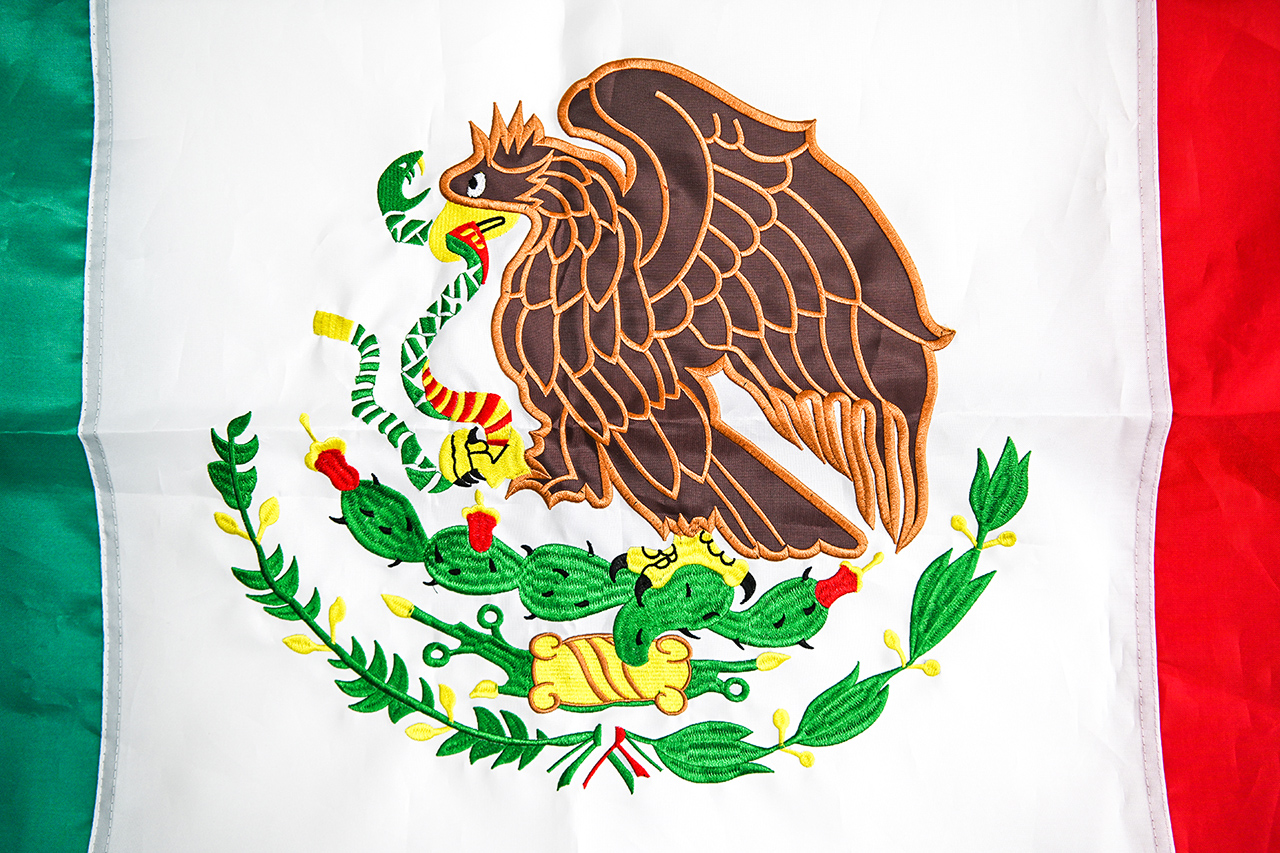 A close-up of a 3x5 custom flag made from 210D polyester, showing the double-stitched hem, reinforced fly end, and vibrant screen-printed design against a clear blue sky