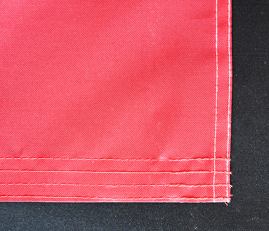 Close-up comparison of a sewn flag’s double-stitched seams versus a dye-sublimated flag’s smooth print surface, highlighting craftsmanship details
