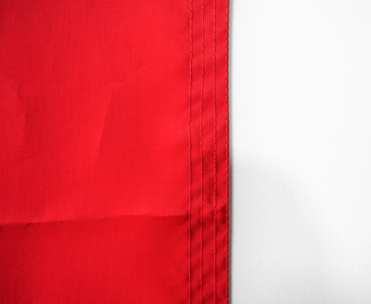 An infographic showing a windspeed chart with recommended flag materials (nylon for light wind, polyester for strong wind) and a diagram of reinforced stitching and canvas header construction.