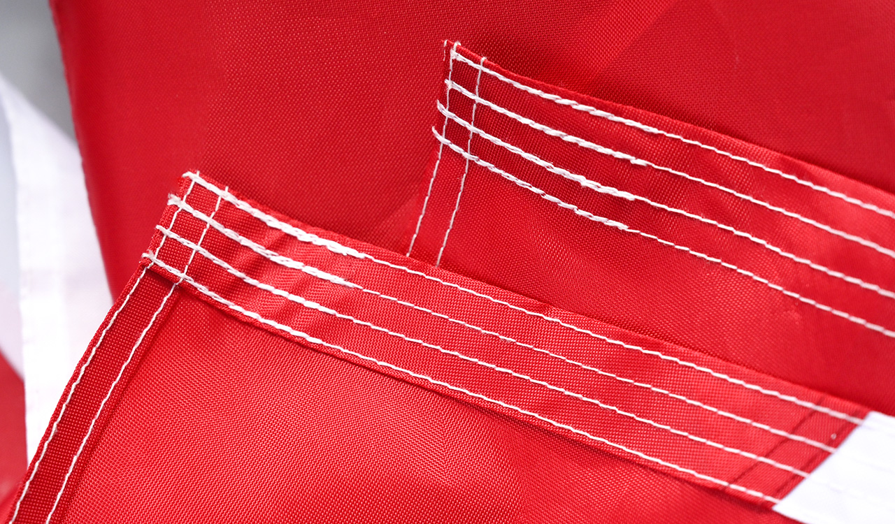 Close-up shot of a multi-head embroidery machine stitching a detailed golden dragon design onto a red polyester flag, with spools of thread in the background at FlagsWin factory