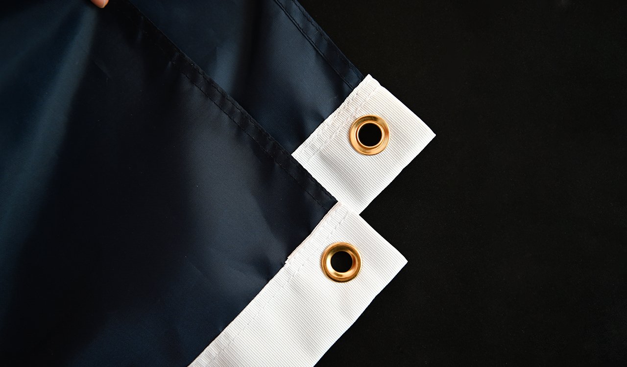 A close-up of a custom 3x5ft polyester flag with vibrant colors and a double-stitched hem, displayed on a flagpole against a clear blue sky.