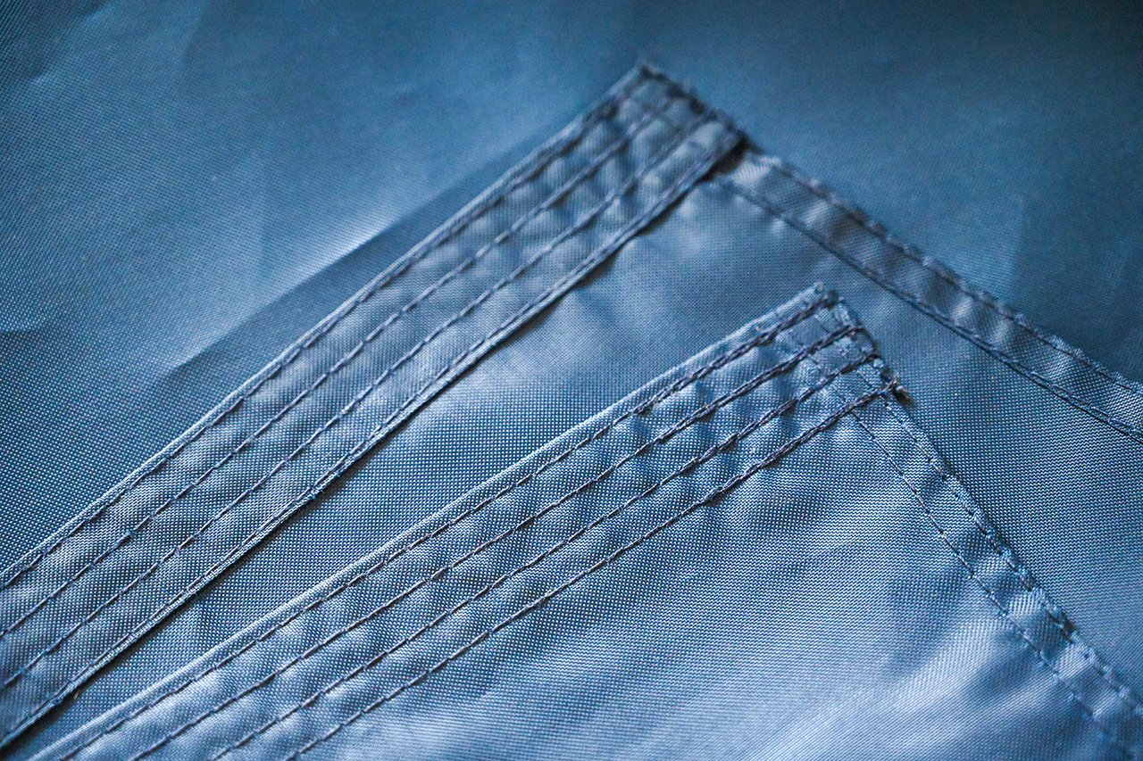 Close-up of a flag sample being measured and checked by hand against a written specification sheet on a table, showing hem stitching and grommet finishing detail