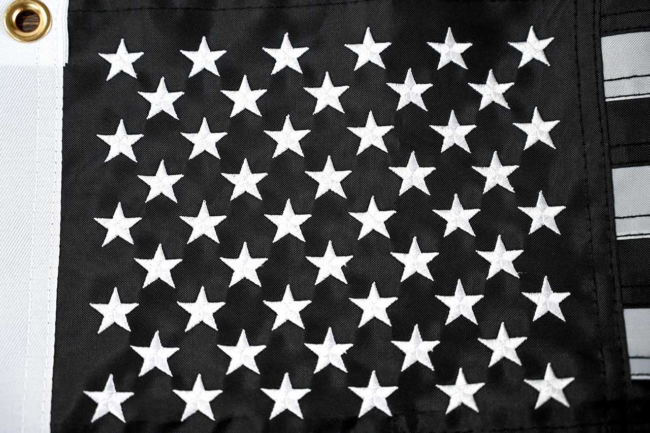 Close-up of a flag laid flat next to an approved printed colour reference under neutral light, showing print registration and edge sharpness